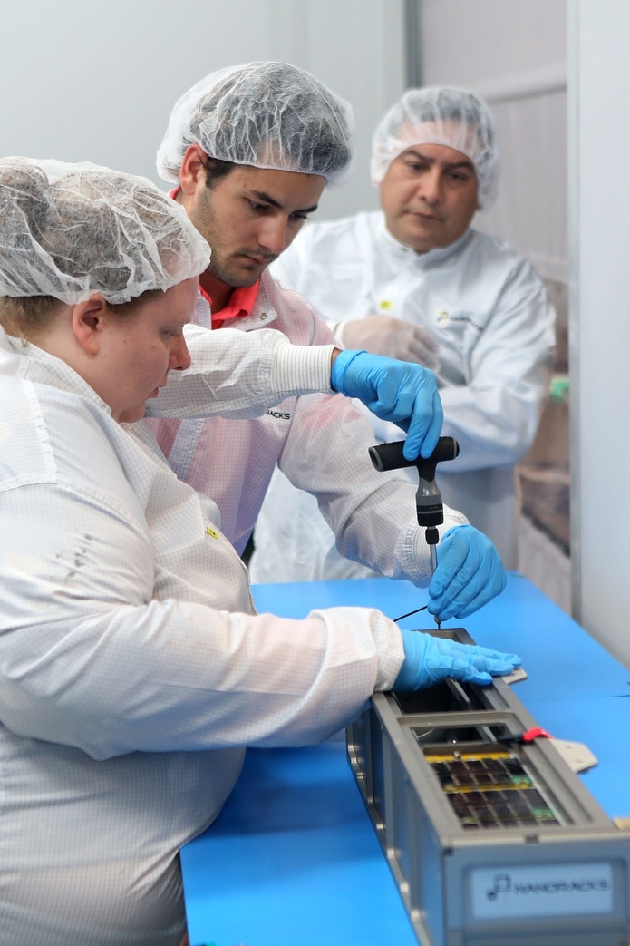 Nanoracks mission manager Jake Cornish and Julia Wolfenbarger are carrying out work on the container that will carry the Puerto Rican satellite PR-CuNaR2.  Note in the background the professor at the College of Engineering at the Bayamón Campus of the Inter-American University in Puerto Rico, Dr. Amilcar Rincón Charris.