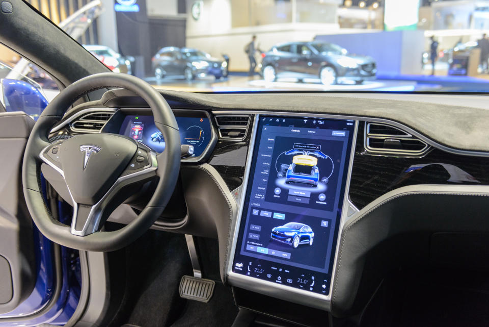 BRUSSELS, Belgium - January 13, 2017: The luxury interior of the Tesla Model X 90D luxury electric SUV SUV with large touchscreen display and dashboard.  The car has leather seats and aluminum details.  The Model X uses falcon wing doors to access the second and third row seats.  The car is displayed on the car display, with the lights off the body.  There are people looking around and other cars displayed in the background.