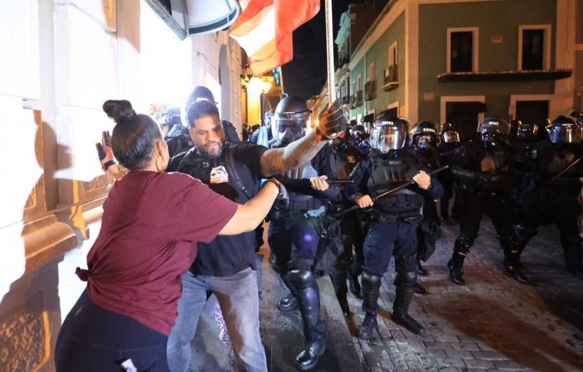 A protester is held by someone else while police advance in the background.