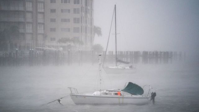 A boat in the middle of a marina is barely visible due to fog caused by strong winds and rain.