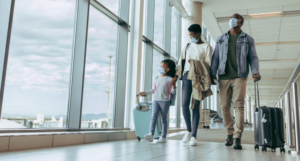 An African family carrying luggage walks by the window in the airport terminal and watches the planes through the glass window.  A family walking through the airport runway.